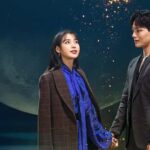 IU y su coprotagonista tomados de la mano frente a una luna gigante en una atmósfera mágica y nocturna con partículas brillantes.