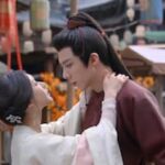 Pareja protagonista de un drama histórico coreano compartiendo un momento íntimo en un mercado tradicional.