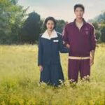 Los actores IU y Park Bo-gum posan juntos en un campo de flores amarillas vistiendo ropa de estilo retro.